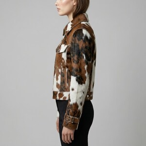 Puede incluir: Una chaqueta de piel de vaca marr&oacute;n, negra y blanca con cuello cl&aacute;sico, dos bolsillos en el pecho y pu&ntilde;os abotonados. La chaqueta tiene un ribete de cuero marr&oacute;n y cierre de bot&oacute;n. La chaqueta se lleva con pantalones negros.