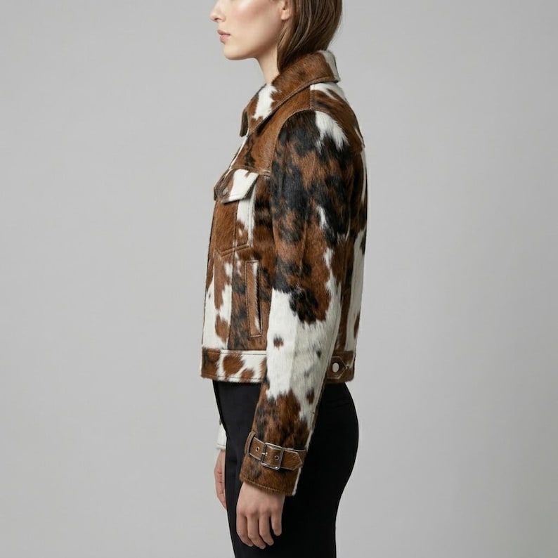 Puede incluir: Una chaqueta de piel de vaca marr&oacute;n, negra y blanca con cuello cl&aacute;sico, dos bolsillos en el pecho y pu&ntilde;os abotonados. La chaqueta tiene un ribete de cuero marr&oacute;n y cierre de bot&oacute;n. La chaqueta se lleva con pantalones negros.