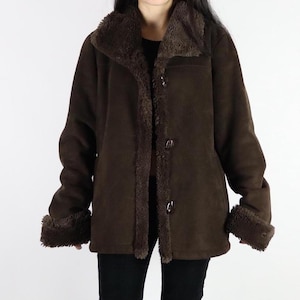 May include: A brown suede coat with a faux fur collar, cuffs, and lining. The coat has a button-up front and long sleeves. The coat is a medium length and appears to be a vintage style.