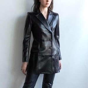 May include: A black leather double-breasted blazer with a notched lapel and two front pockets. The blazer has long sleeves and a tailored fit. The model is wearing black leather pants. The outfit is a classic, stylish look.