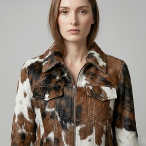 Puede incluir: Chaqueta de piel de vaca marr&oacute;n, negra y blanca con cierre de cremallera y dos bolsillos en el pecho. La chaqueta tiene un cuello cl&aacute;sico y un patr&oacute;n natural y texturizado. Es una prenda llamativa.