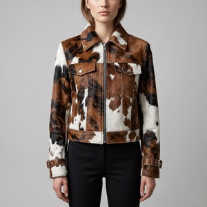 Puede incluir: Chaqueta corta de piel de vaca con un estampado de manchas marrones, negras y blancas. La chaqueta tiene cuello, dos bolsillos en el pecho y cremallera. Las mangas tienen pu&ntilde;os ajustables con hebillas. La chaqueta se lleva con pantalones negros.