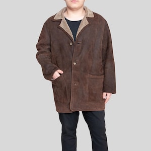 K&ouml;nnte beinhalten: Ein brauner Wildledermantel mit Shearling-Kragen und -Futter. Der Mantel hat eine Knopfleiste, zwei Vordertaschen und eine lockere Passform. Ein warmes Oberbekleidungsst&uuml;ck.