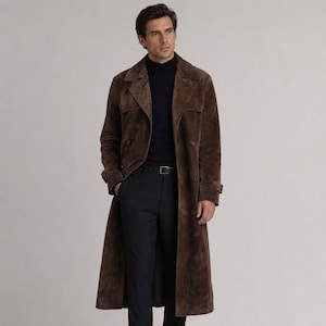 May include: A long, double-breasted brown suede trench coat featuring wide lapels, long sleeves with buckled cuffs, and a structured silhouette. The coat is worn over a black turtleneck sweater and dark trousers with a black leather belt.