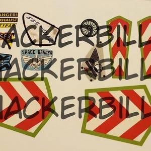 May include: A collection of colorful stickers and patches featuring designs from the movie Toy Story. Includes text that reads "DANGER! JET EXHAUST LIGHTYEAR LASER" and "SPACE RANGER". Also includes red and white chevron designs.