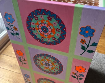 Puede incluir: Un mueble de madera pintado a mano con un diseño floral. El mueble presenta una combinación de colores rosa, morado y verde, con patrones de mandala circulares y detalles de flores. La parte superior del mueble está llena de monedas.