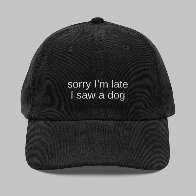 May include: Black corduroy baseball cap with the embroidered text "sorry I'm late I saw a dog" in white. The cap has a curved brim and an adjustable strap at the back.