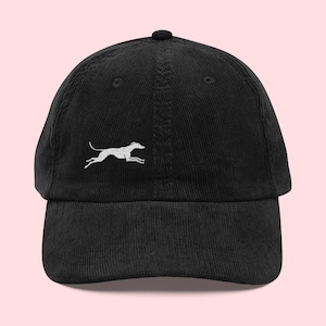 May include: Black corduroy baseball cap with a white embroidered running dog design. The cap has a curved brim and an adjustable strap at the back. A stylish accessory for casual wear.