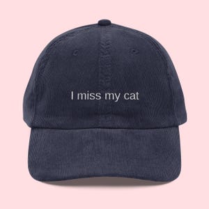 May include: Navy blue corduroy baseball cap with the embroidered text "I miss my cat" in white. The cap has a curved peak and a fabric-covered button. A casual accessory for cat lovers.