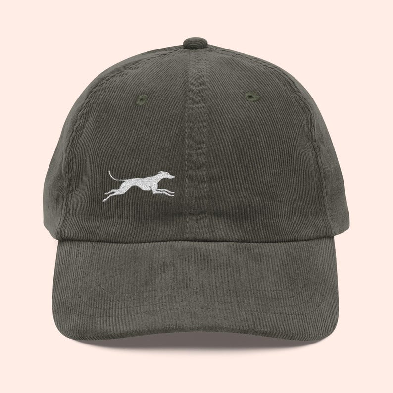 May include: Olive green corduroy baseball cap featuring a white embroidered running dog design. The cap has a curved brim and an adjustable strap at the back. A stylish accessory for casual wear.