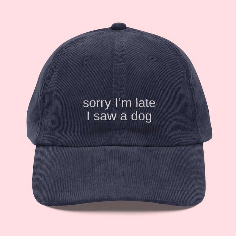 May include: Navy blue corduroy baseball cap with the embroidered text "sorry I'm late I saw a dog". The cap has a curved brim and a top button.