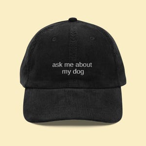 May include: Black corduroy baseball cap with the text "ask me about my dog" embroidered in white. The cap has a curved brim and an adjustable strap. A casual accessory for dog lovers.
