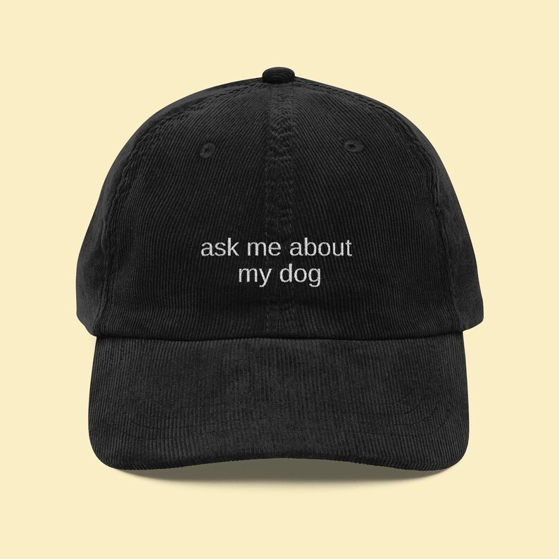 May include: Black corduroy baseball cap with the text "ask me about my dog" embroidered in white. The cap has a curved brim and an adjustable strap. A casual accessory for dog lovers.