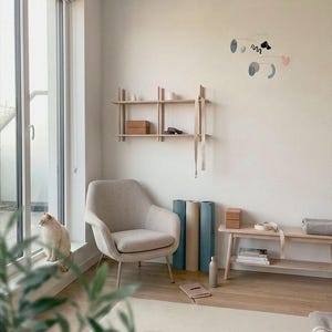 Peut inclure: Int&eacute;rieur serein avec un fauteuil beige, des tapis de yoga et une &eacute;tag&egrave;re en bois. Un chat est assis pr&egrave;s d'une grande fen&ecirc;tre. La pi&egrave;ce est d&eacute;cor&eacute;e dans des tons neutres, cr&eacute;ant une atmosph&egrave;re apaisante. Accessoires de yoga et bouteille d'eau.