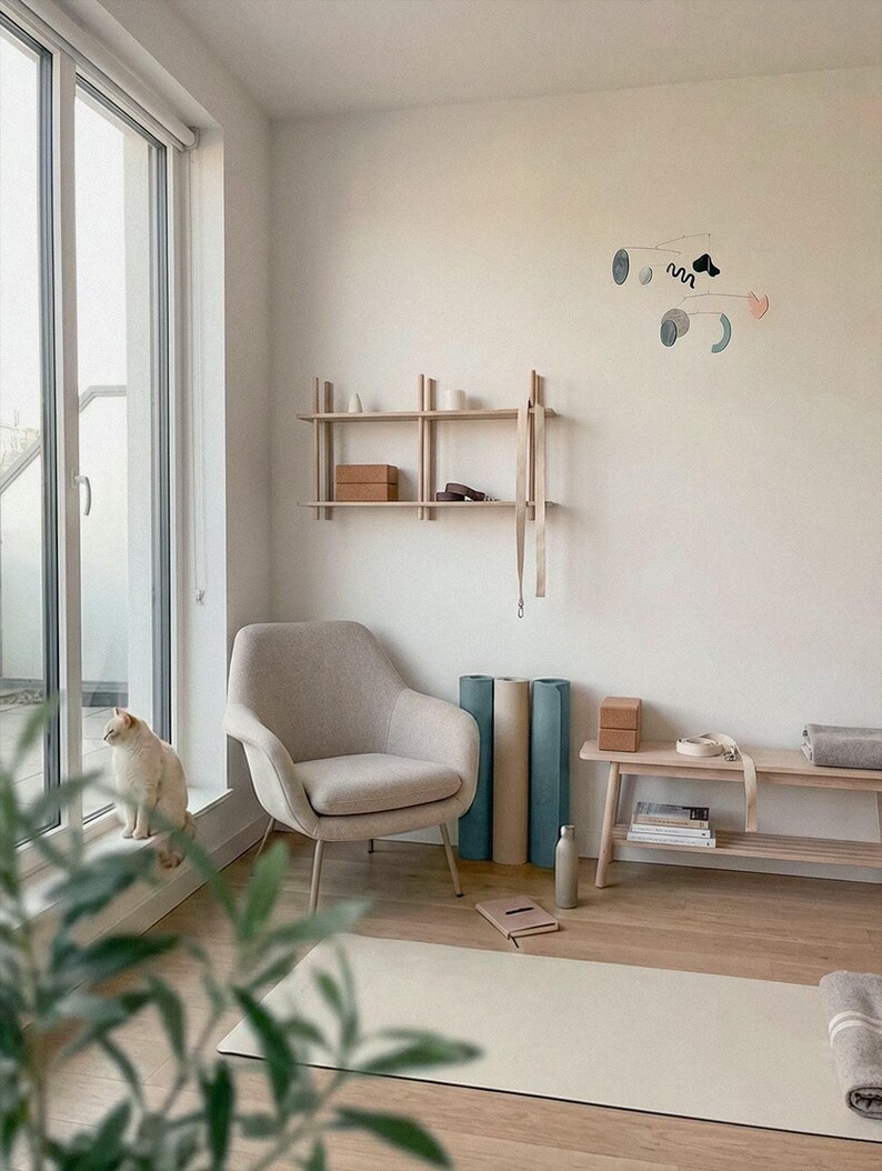 Peut inclure: Int&eacute;rieur serein avec un fauteuil beige, des tapis de yoga et une &eacute;tag&egrave;re en bois. Un chat est assis pr&egrave;s d'une grande fen&ecirc;tre. La pi&egrave;ce est d&eacute;cor&eacute;e dans des tons neutres, cr&eacute;ant une atmosph&egrave;re apaisante. Accessoires de yoga et bouteille d'eau.