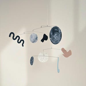 Peut inclure: Mobile artistique avec des formes abstraites et des &eacute;l&eacute;ments circulaires. Le mobile pr&eacute;sente des couleurs vari&eacute;es, dont le noir, le blanc et le bleu. Le design comprend une forme ondul&eacute;e, une main et un &eacute;l&eacute;ment bleu incurv&eacute;.