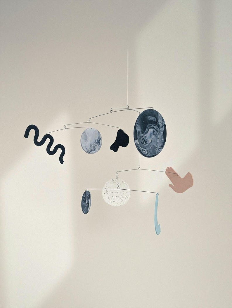 Peut inclure: Mobile artistique avec des formes abstraites et des &eacute;l&eacute;ments circulaires. Le mobile pr&eacute;sente des couleurs vari&eacute;es, dont le noir, le blanc et le bleu. Le design comprend une forme ondul&eacute;e, une main et un &eacute;l&eacute;ment bleu incurv&eacute;.