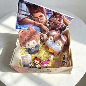 May include: A gift box containing two plush dolls with animal ears, one wearing a grey suit and the other with brown fur and glasses. The box includes several small character cards, two acrylic keychains featuring anime-style figures, and a large rectangular print of a character with red hair and glasses.