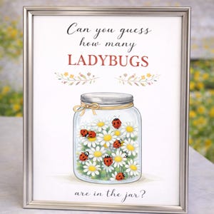 Op de afbeelding: Ingelijste print met een pot gevuld met madeliefjes en lieveheersbeestjes. Tekst: "Can you guess how many LADYBUGS are in the jar?" De pot heeft een zilveren deksel en een gouden lint. De lijst is zilver.