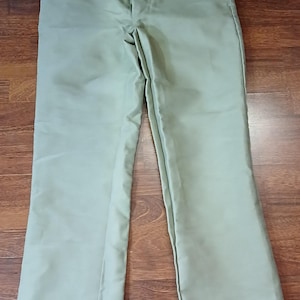 May include: Khaki-colored pants with a straight leg design. The pants are made of a durable fabric and feature a button and zipper closure. The pants are laid flat on a wooden surface.