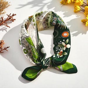 Puede incluir: Un pañuelo cuadrado de seda con un diseño botánico. El pañuelo presenta una mezcla de colores verdes, blancos y beige con estampados florales y geométricos. El pañuelo está anudado, mostrando sus diversos diseños.