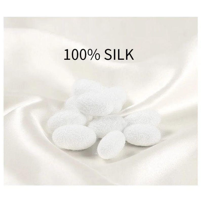 May include: A collection of white silk cocoons, with a textured surface, are arranged on a white, silky fabric. The text "100% SILK" is displayed above the cocoons. The image has a soft, bright appearance.