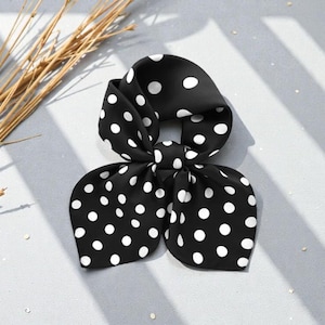 May include: A black hair bow with white polka dots. The bow is tied in a decorative knot, with the ends fanning out. The accessory is made of a silky material and is suitable for various hairstyles.