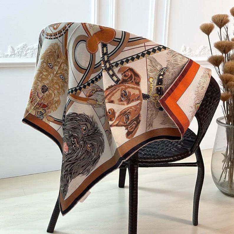 May include: A silk scarf draped over a chair, featuring a repeating pattern of dog portraits in shades of brown, beige, and black. The scarf has a contrasting orange and brown border and is decorated with equestrian-themed elements.
