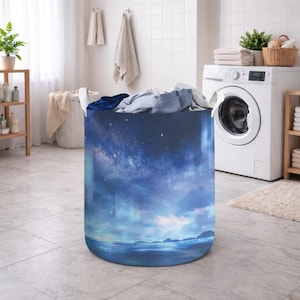May include: A cylindrical laundry hamper with a celestial design featuring a starry night sky, clouds, and a body of water. The hamper is filled with folded clothes and is in a laundry room setting.