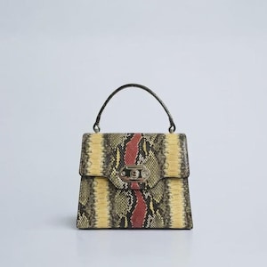 Peut inclure: Sac à main carré avec un motif peau de serpent jaune, noir et rouge. Le sac est doté d'une poignée noire et d'un fermoir argenté. Le motif serpentin est vertical avec une bande rouge au centre.