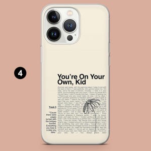 May include: Cream-colored phone case with a black and white floral design and the text "You're On Your Own, Kid." The case has a clear, glossy finish and a camera cutout. The phone case is designed to fit a smartphone.