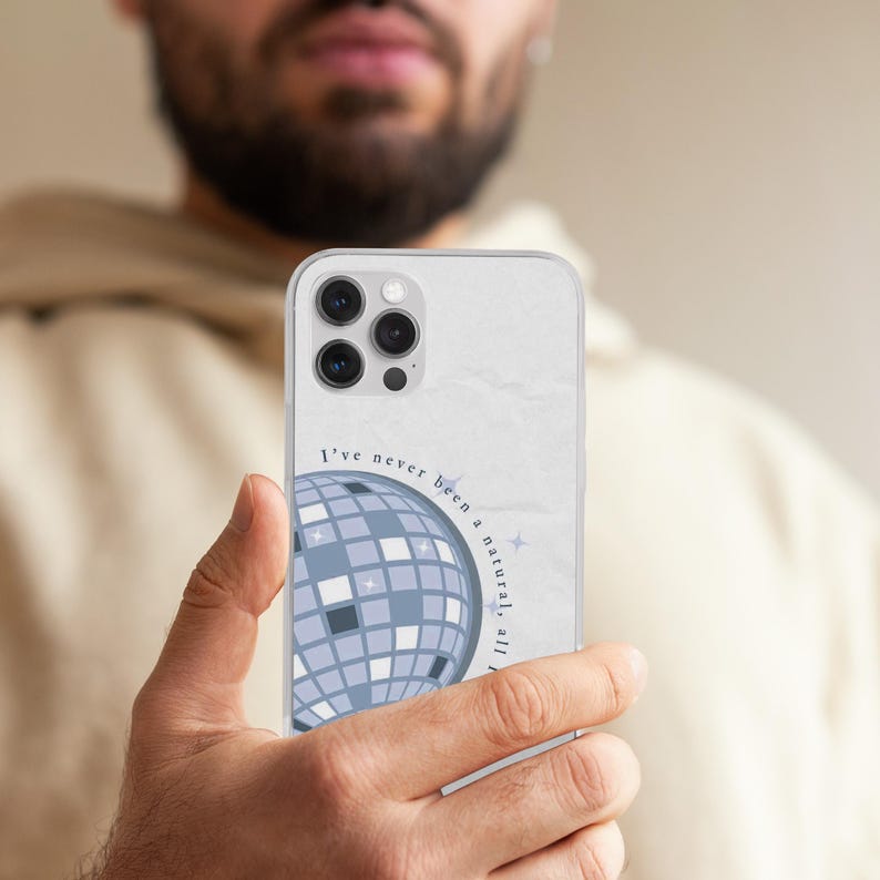 May include: A clear phone case featuring a disco ball graphic in shades of blue and gray. The case has the text "I've never been a natural, all I do is shine." The phone case is held by a person.