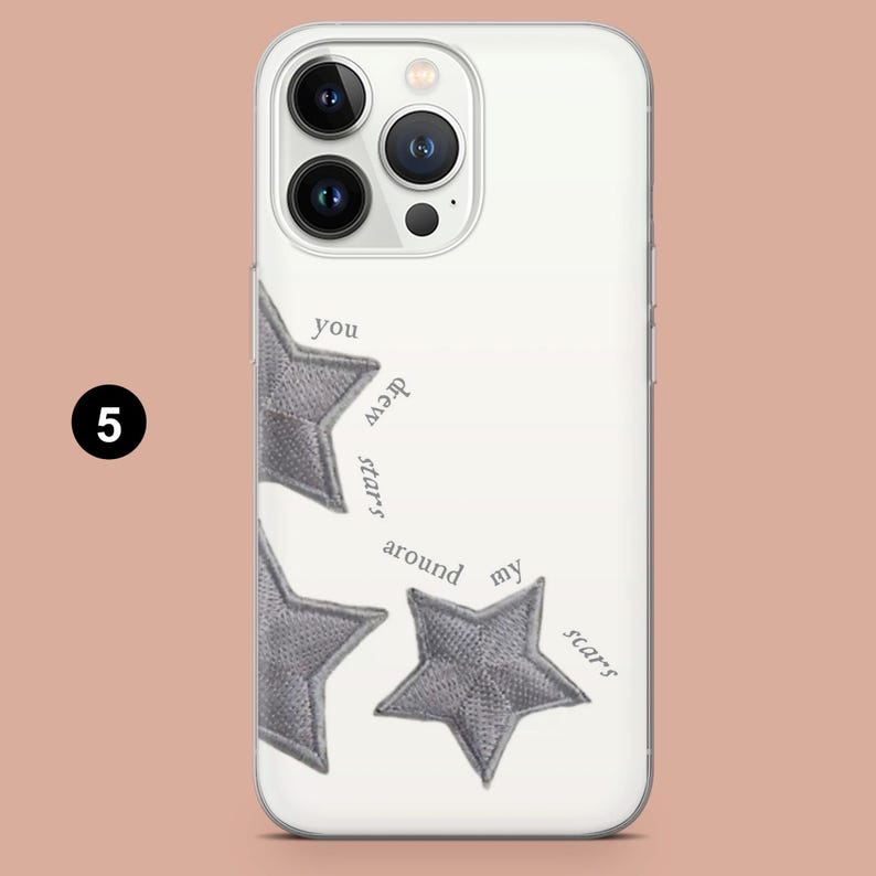 May include: White phone case with a design featuring three gray embroidered stars and the text "you drew stars around my scars". The case has a clear border and covers the back and sides of the phone.