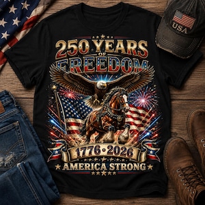 May include: A black t-shirt featuring a graphic print of a bald eagle flying above a brown horse, with an American flag background, fireworks, and the text 250 YEARS OF FREEDOM 1776-2026 AMERICA STRONG in gold, red, white, and blue lettering.