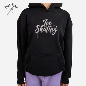 Könnte beinhalten: Ein schwarzer Kapuzenpullover mit einer Kängurutasche vorne und dem Text Ice Skating in einer silbernen, glitzernden und tropfenden Schriftart. Das Logo bestickt mit einem Nadel- und Faden-Symbol ist oben links im Bild zu sehen.