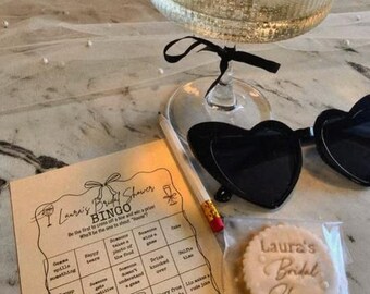 May include: A bridal shower scene with a champagne-filled glass, heart-shaped sunglasses, a bingo game, a pencil, and a cookie. The bingo card reads "Laura's Bridal Shower BINGO". The cookie is inscribed with "Laura's Bridal Shower".