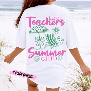 Può includere: T-shirt bianca con grafica a tema spiaggia in rosa e verde. Il design include un ombrellone, una sedia a sdraio e le parole "Teachers Summer Club". Il testo "2 Color Options" è in basso.