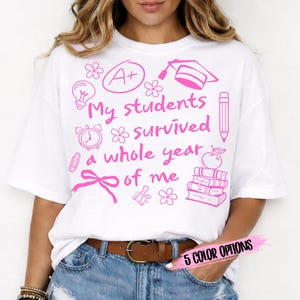 Puede incluir: Camiseta blanca con un gráfico rosa que dice "My students survived a whole year of me". El diseño incluye un gorro de graduación, lápiz, libros y otros iconos escolares. También es visible el texto "5 COLOR OPTIONS".