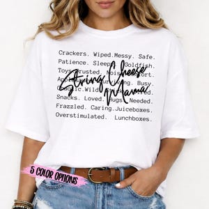 May include: White t-shirt with the words "String Mama" in a handwritten font. The shirt also has a list of words like "Crackers," "Messy," and "Lunchboxes." The text "5 COLOR OPTIONS" is at the bottom.