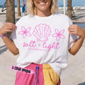 May include: White t-shirt with a pink seashell, flowers, and text that reads "salt + light" and "Matthew 5:13-16". The shirt also has "5 COLOR OPTIONS" printed on it.