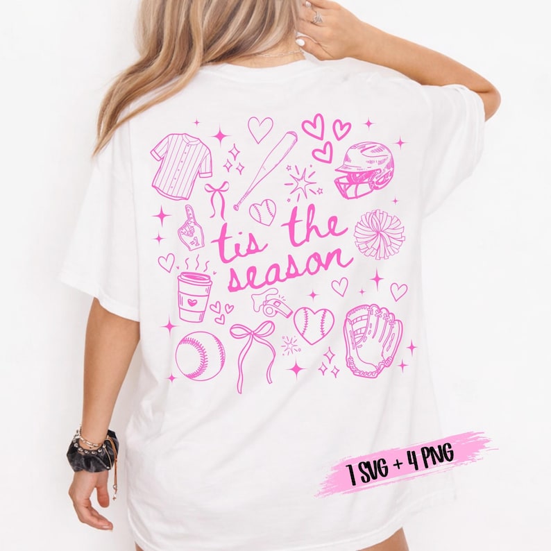 May include: White t-shirt with a pink baseball-themed graphic on the back. The design includes a baseball jersey, bat, helmet, glove, ball, and the phrase "tis the season". Additional elements include hearts, bows, and a coffee cup.