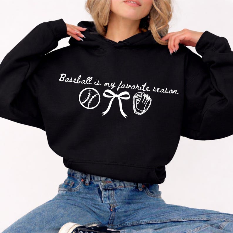 May include: Black hoodie with white text and baseball-themed graphics. The text reads "Baseball is my favorite season" with a baseball, bow, and baseball glove graphic. A casual, comfortable sweatshirt.