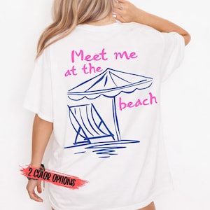 May include: White t-shirt with a beach-themed graphic. The design features a beach umbrella, a lounge chair, and the text "Meet me at the beach" in pink and blue. The bottom of the shirt has a red banner that says "2 COLOR OPTIONS".