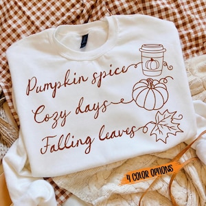 May include: A white crewneck sweatshirt featuring brown text that reads Pumpkin spice, Cozy days, and Falling leaves. The design includes a line-art graphic of a coffee cup with a pumpkin, a whole pumpkin, and a maple leaf. The text 4 COLOR OPTIONS is visible.