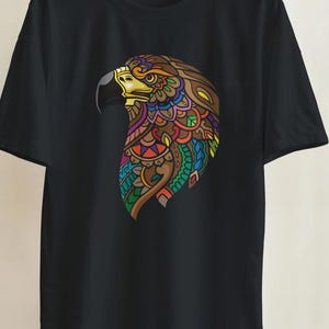 May include: A black short-sleeved t-shirt featuring a detailed graphic of an eagle head on the chest. The eagle design is composed of intricate, colorful patterns in shades of orange, red, green, blue, and yellow, with a prominent yellow beak.