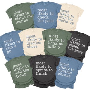 May include: A collection of ten short-sleeved t-shirts in various colors, each with the phrase "most likely to" followed by a different running-related activity printed in white. Colors include green, blue, black, and beige.