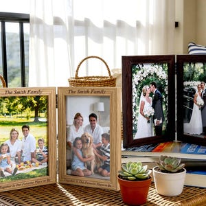 May include: Three wooden photo frames with family photos and the text "The Smith Family". One frame is a two-panel design. The frames are on a woven table with small potted plants and a basket.