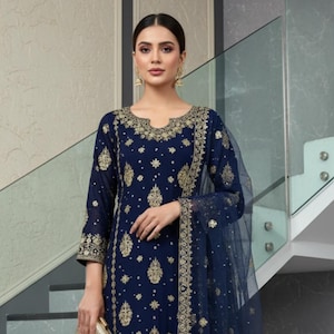 Può includere: Un salwar kameez blu navy ricamato con dettagli dorati. L'outfit include un dupatta e pantaloni abbinati. L'immagine mostra anche una pochette dorata e il testo "kridha FASHION".