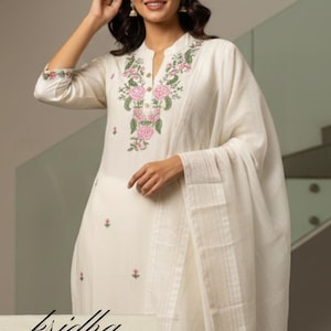 K&ouml;nnte beinhalten: Cremefarbenes besticktes Kurta-Set mit passendem Dupatta. Der Kurta hat einen Stehkragen und florale Stickereien in Rosa und Gr&uuml;n. Der Text "kridha FASHION" ist unten im Bild zu sehen.