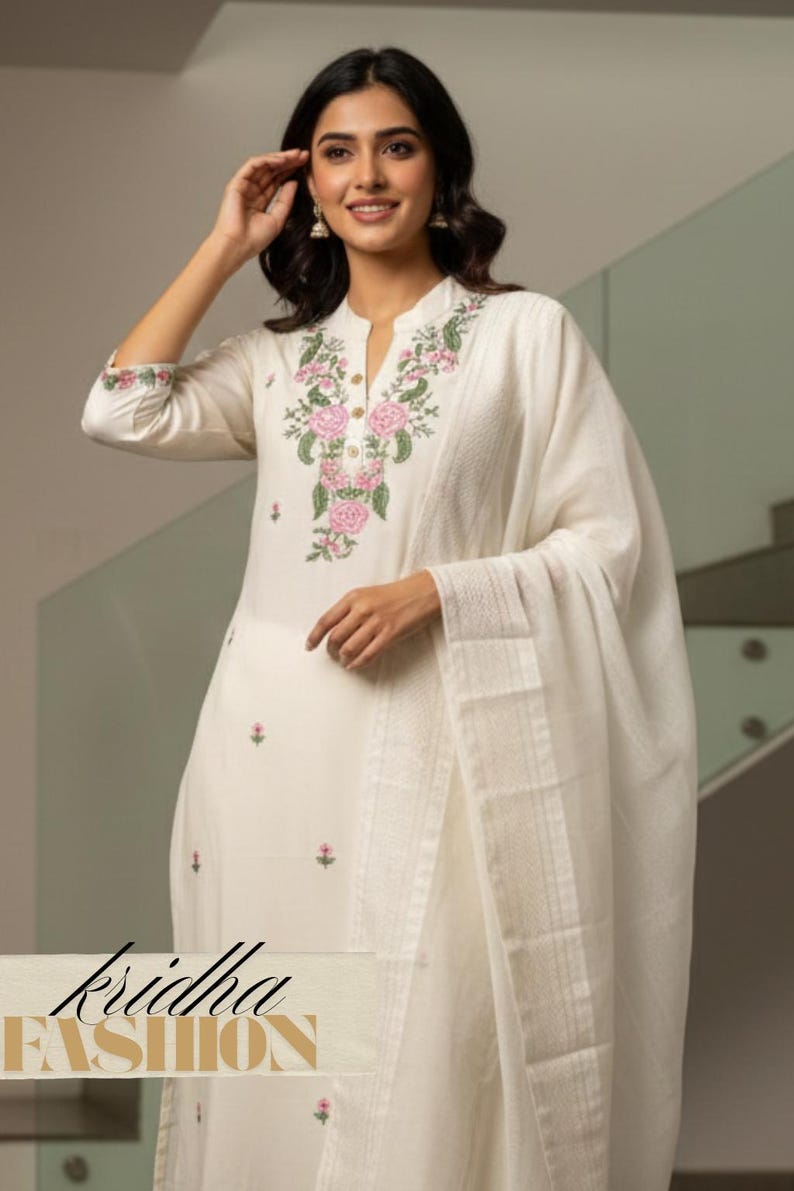 K&ouml;nnte beinhalten: Cremefarbenes besticktes Kurta-Set mit passendem Dupatta. Der Kurta hat einen Stehkragen und florale Stickereien in Rosa und Gr&uuml;n. Der Text "kridha FASHION" ist unten im Bild zu sehen.